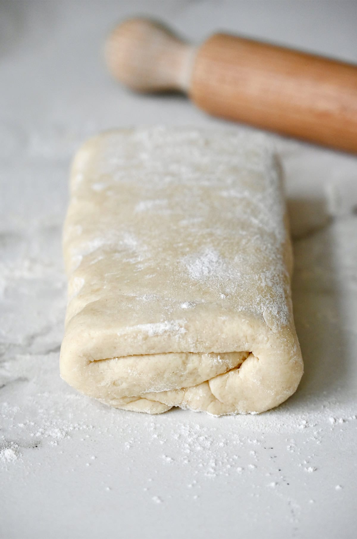 Folded pie dough that resembles a folded letter on a floured surface.