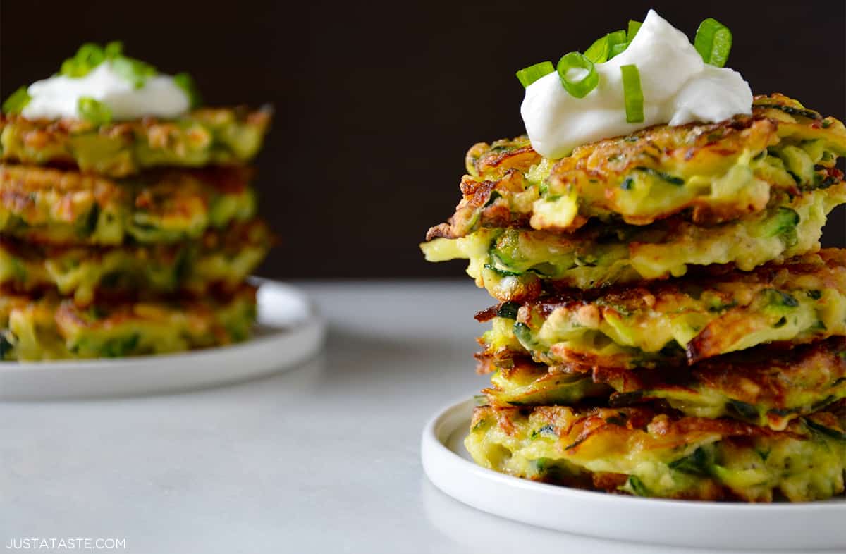 Two tall stacks of crispy zucchini fritters topped with a dollop of sour cream and sliced scallions.