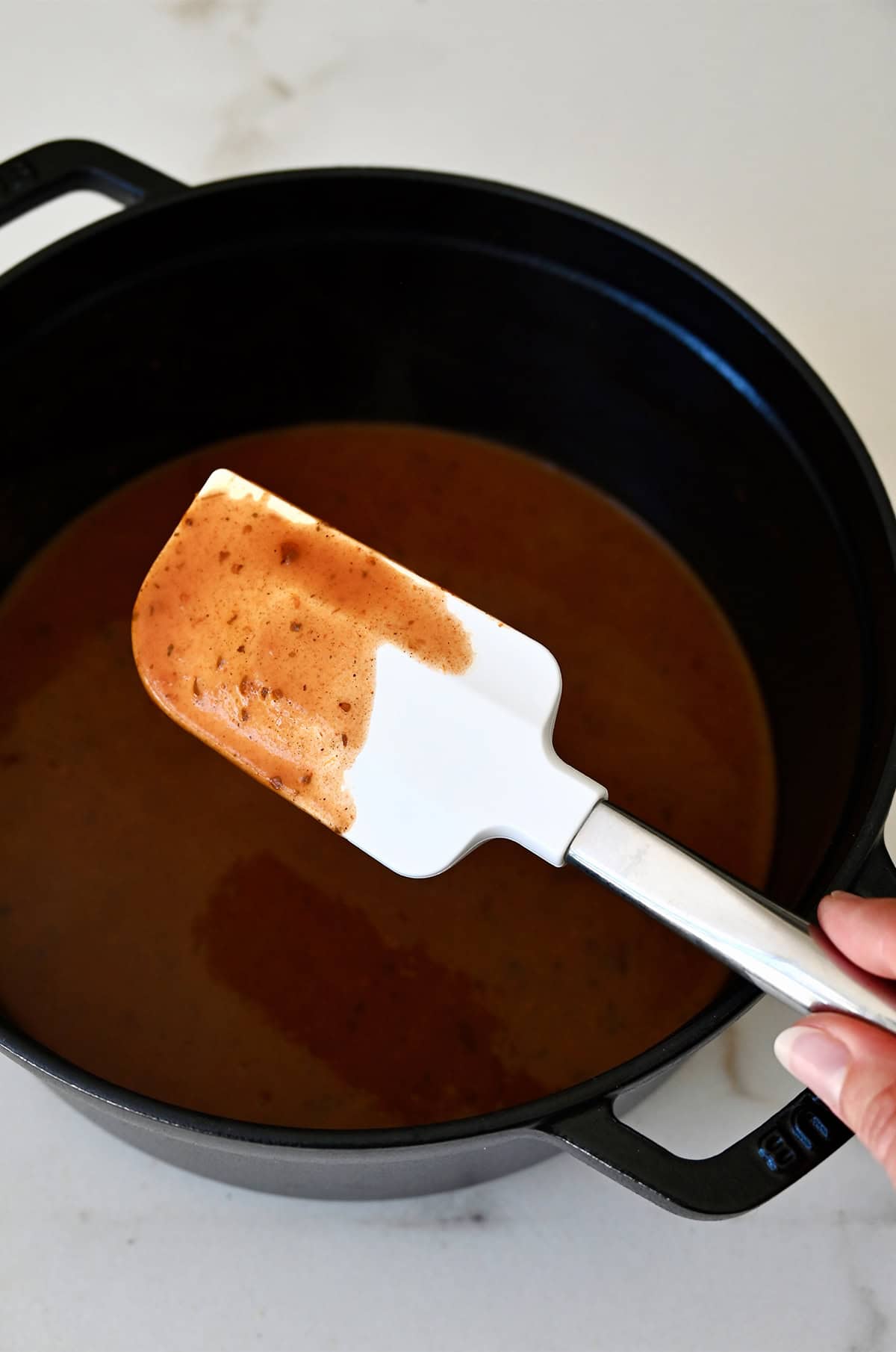 Homemade enchilada sauce covering a spatula above a sauté pan with more sauce.