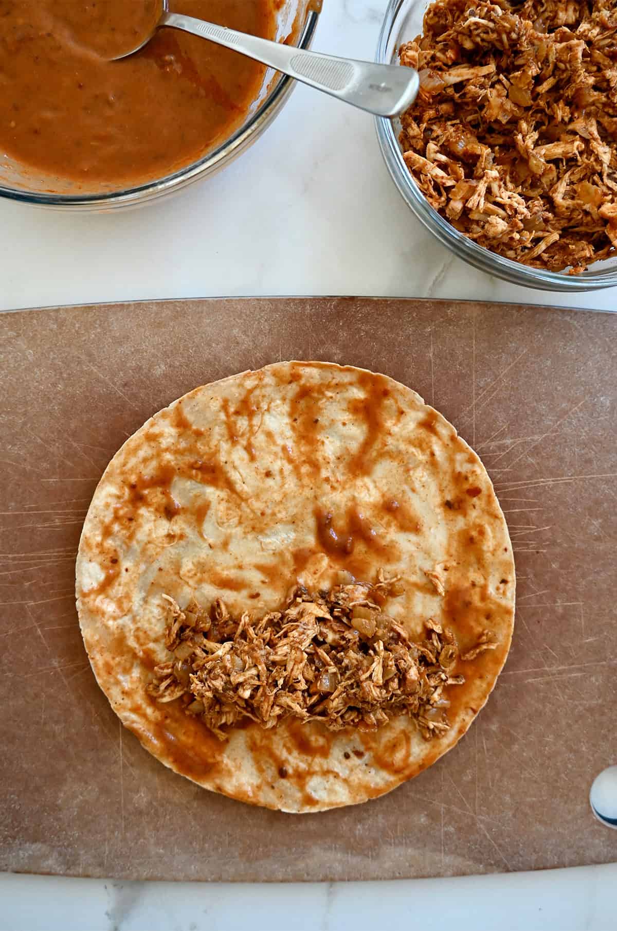 Shredded chicken filling atop a tortilla that's been dipped into enchilada sauce.