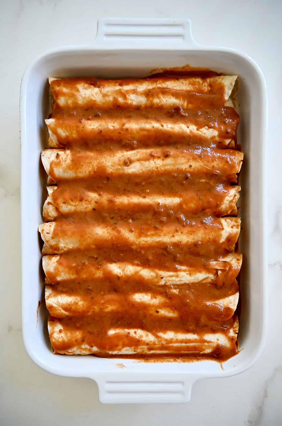 A single layer of enchiladas covered with homemade enchilada red sauce in a 9x13 baking dish.