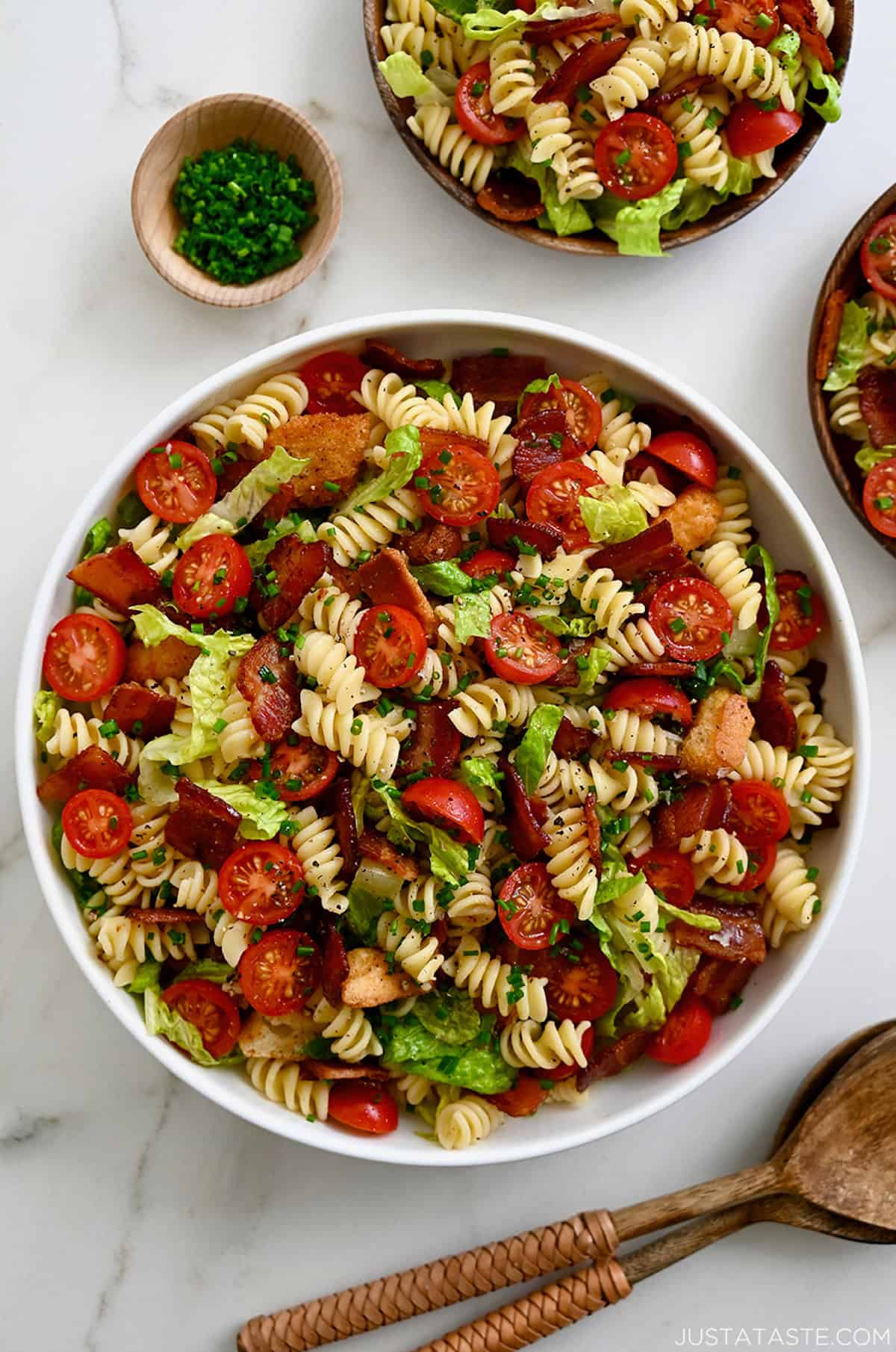 BLT pasta salad in a large serving bowl next to wood serving spoons.
