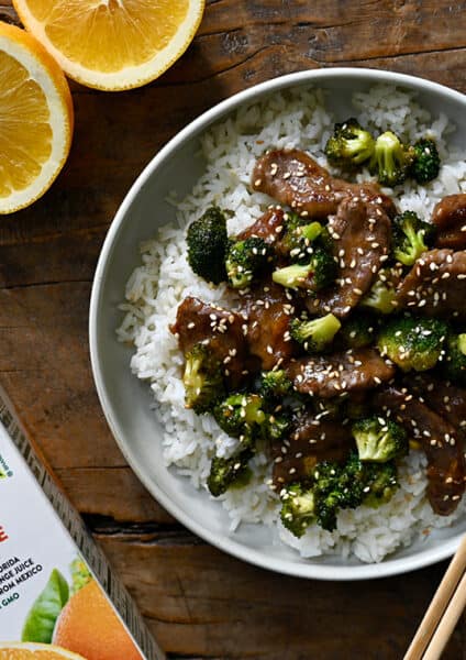 A top down view of Orange Beef and Broccoli in a bowl with chopsticks and sliced oranges next to it