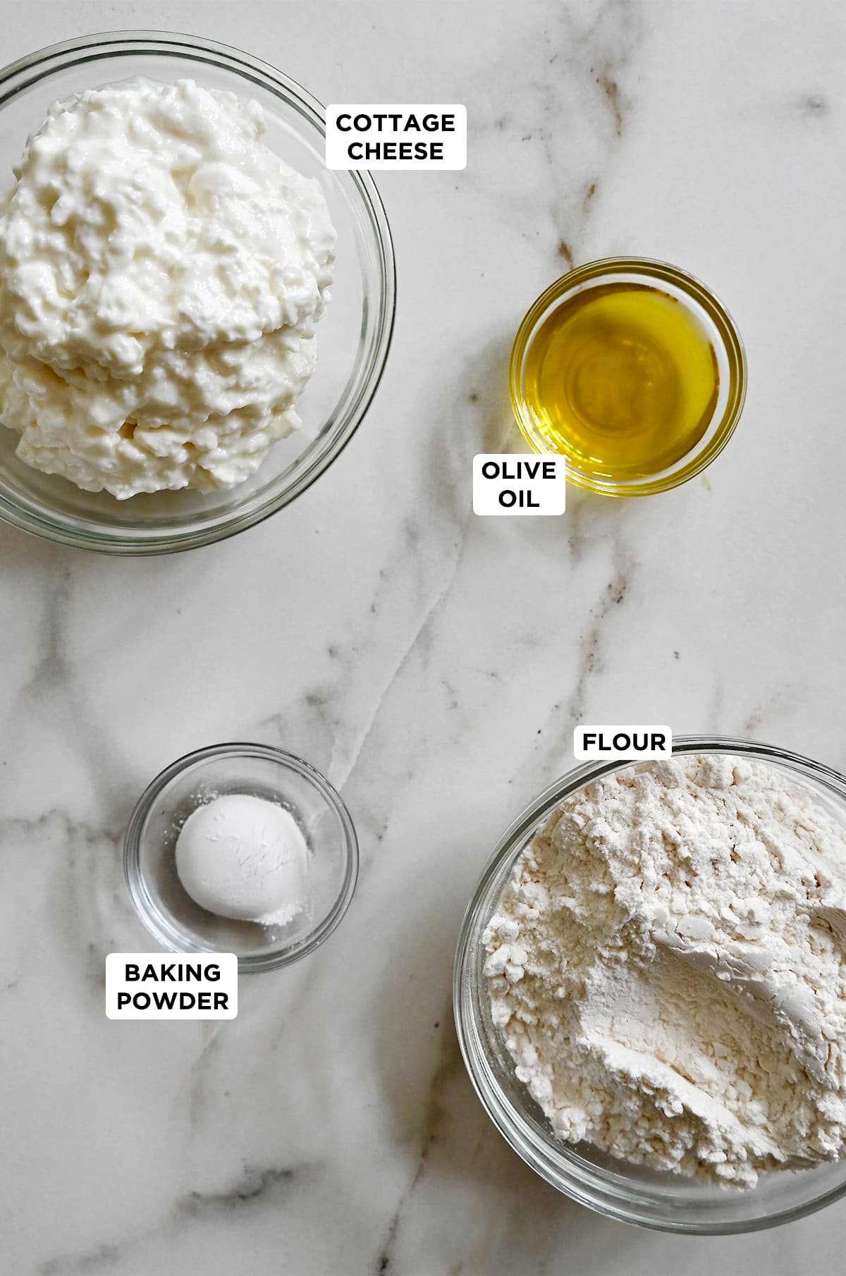 Glass bowls containing ingredients to make cottage cheese pizza dough: Flour, cottage cheese, olive oil and baking powder.