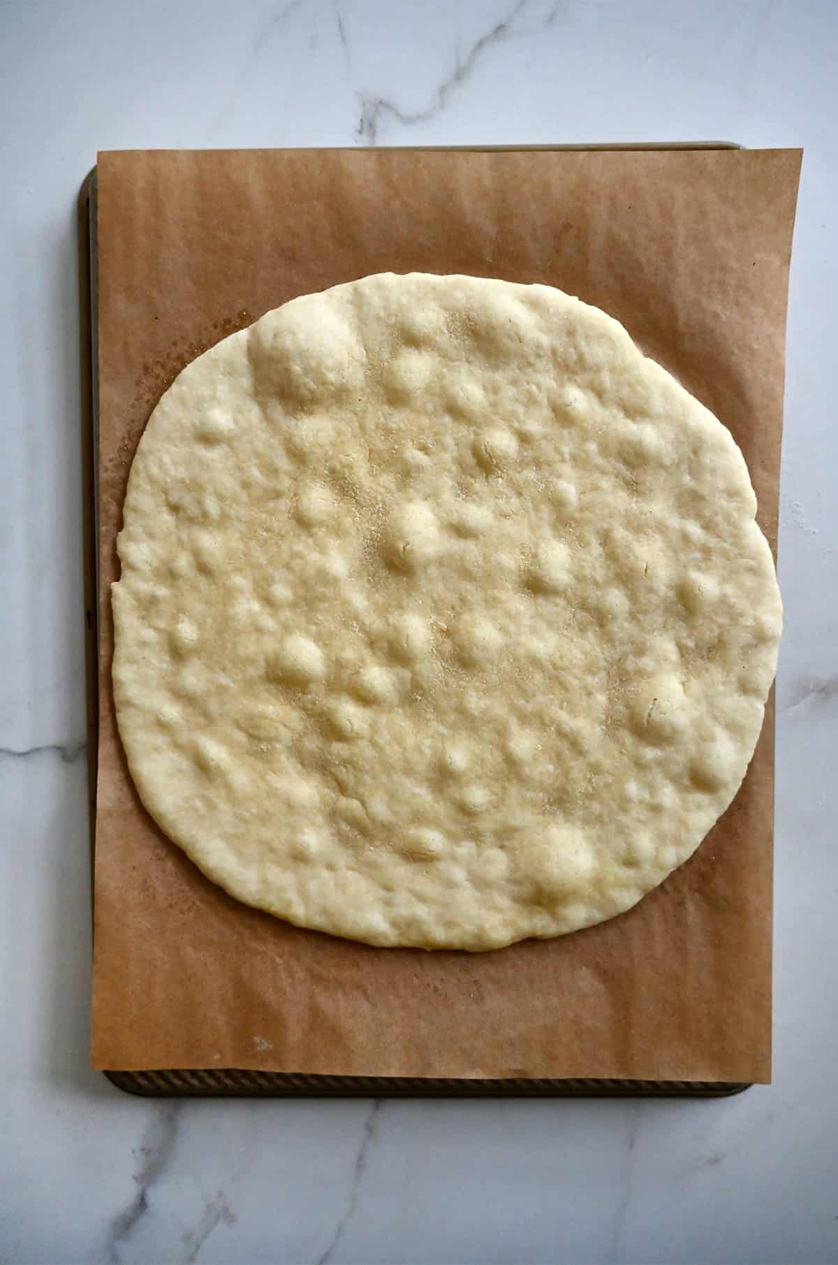 Par baked cottage cheese pizza crust on a parchment paper-lined baking sheet.