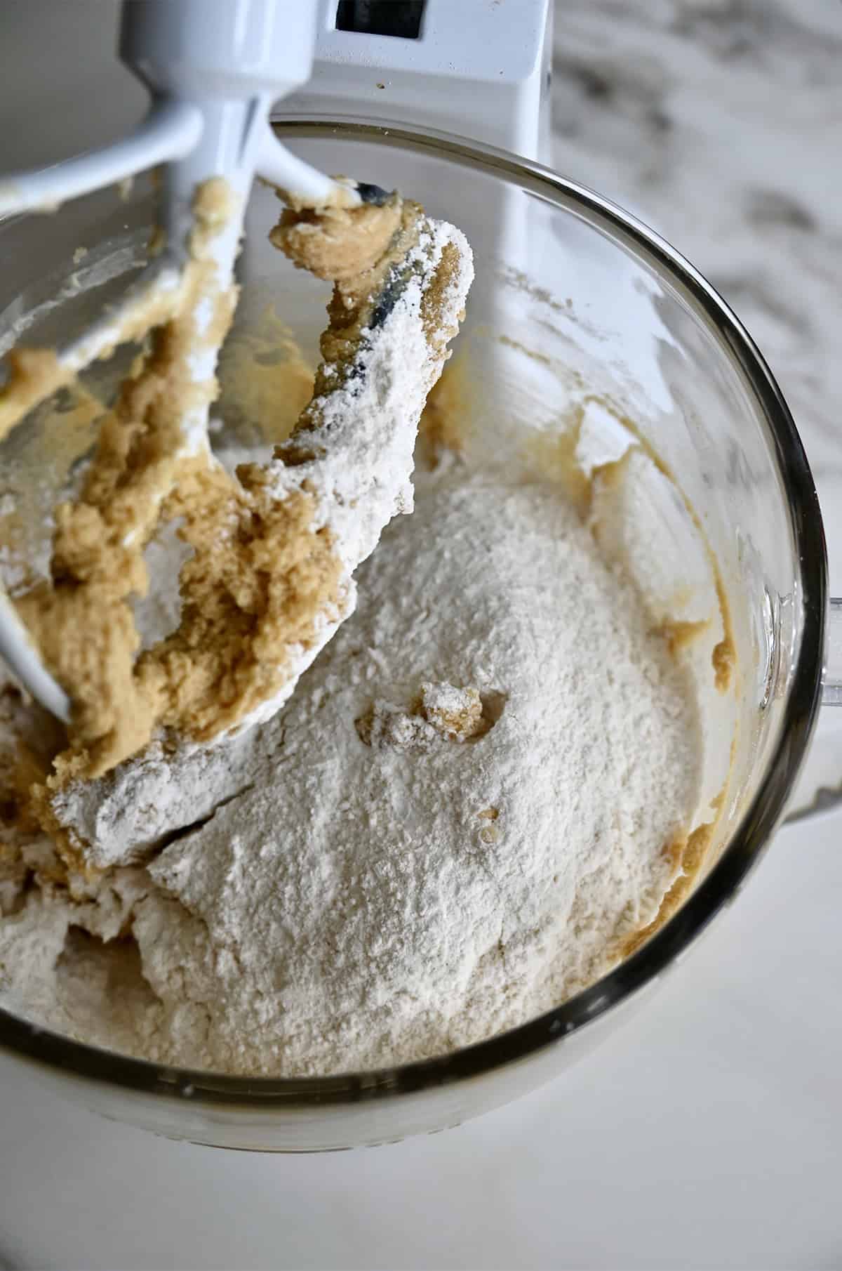 Adding dry ingredients to a large mixing bowl with creamed butter, sugar, eggs and vanilla extract.